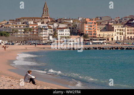 A woman sits contemplating on the beach of Palamos, Catalunya, Spain Stock Photo