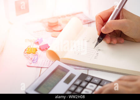 Hand writing and counting on calculator in office on wood desk about financial data analyzing, Choose focus point. In over light. Stock Photo