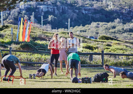 Actors Jake Ryan and Sam Frost plus extras film an outdoor scene of a  training session for the Home & Away tv series at Palm Beach, Australia Stock Photo