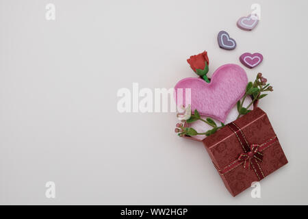 Heart-shaped pillow and mini flower in gift box on pink background, valentine concept. Stock Photo