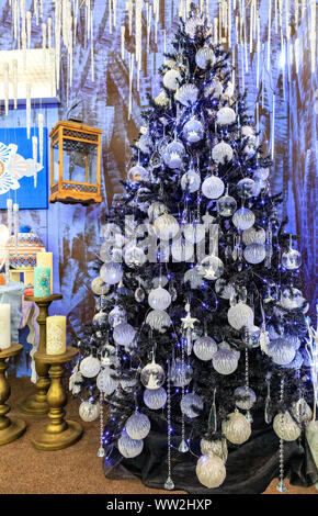 A collection of silver stars, Christmas balls, Christmas baubles, decorative icicles is illuminated by blue lights on a slender Christmas tree. Stock Photo