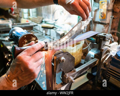 sharpening Khukur traditional Nepali knife on grinding machine in rural workshop Stock Photo