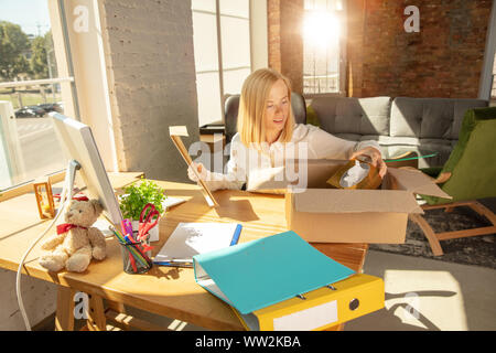 A young businesswoman moving in the office, getting new work place. Young caucasian female office worker equips new cabinet after promotion. Unpacking boxes. Business, lifestyle, new life concept. Stock Photo