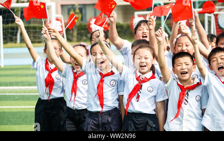 Young Chinese students wave Chinese national flags during a celebration event for the 70th anniversary of the founding of the People's Republic of Chi Stock Photo