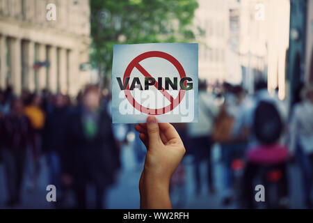 Human hand holding a protest banner stop vaping message over a crowded street background. Banning flavored vaping products to discourage people from s Stock Photo