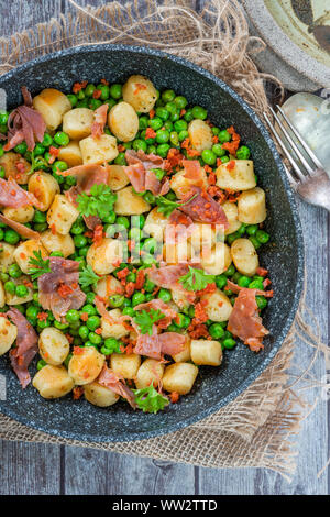 Potato gnocchi with green peas, pesto, proscuitto and chorizo in frying pan - overhead view Stock Photo