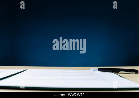 Low angle view of a contract in folder an a pen lying on office desk. Over navy blue background with copy space. Stock Photo