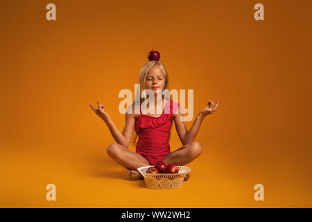 little child girl in a red swimsuit sitting in lotus position on orange background. Stock Photo