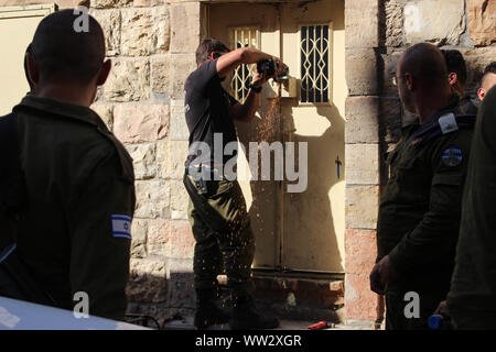 Hebron, West Bank, Palestinian Territory. 12th Sep, 2019. Israeli security forces stand guard as a worker closes a house of a Palestinian man at al-Shuhada street, that Israel unilaterally closed it in 1994, in the West Bank city of Hebron on September 12, 2019. On February 25, 1994, Israeli settler Baruch Goldstein opened fire in the Ibrahimi mosque killing 29 Palestinians in worship. Since then, Shuhada Street, once the main street and marketplace, has remained almost entirely closed to Palestinians. There are 20 checkpoints and front doors to Palestinian shops and homes are sealed shut Stock Photo