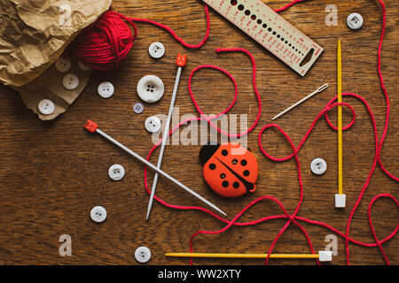 Knitting tools and accessories spilling out from a brown paper bag onto a wooden table top Stock Photo