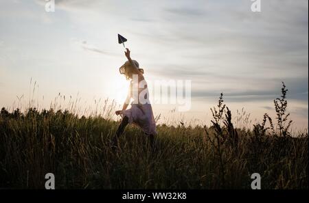 girl chasing a paper aeroplane in a meadow at sunset Stock Photo