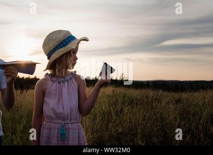 profile of a young girl holding a paper plane in a meadow at sunset Stock Photo