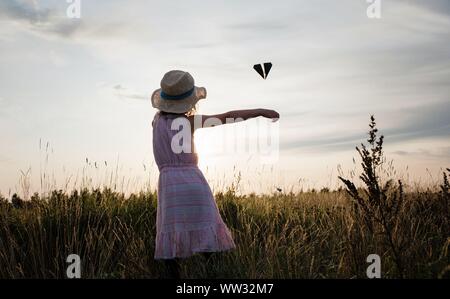 young girl playing with a paper plane in a meadow at sunset in summer Stock Photo