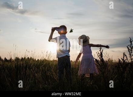 brother and sister flying planes playing in a meadow at sunset