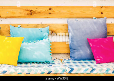 Close up pillows on an outdoor patio chair, with a blue striped cushioned bench. Stock Photo