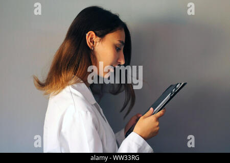 Medicine Concept: Young female doctor on a gray background using a digital tablet. Healthcare technology. Stock Photo