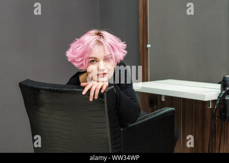 Beautiful hairstyle of young woman after dying hair and making highlights in beauty salon. Close up short pink hairdo Stock Photo