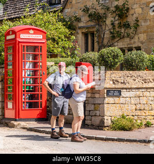 A couple of senior hikers walking the Cotswold Way stop to read the map beside the red telephone box now converted into an information point in the Co Stock Photo