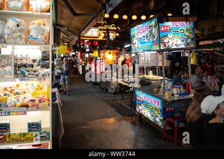 Taipei, Taiwan: Raohe night market stalls at night with blurry background with shop selling toys and plush toys on the left Stock Photo