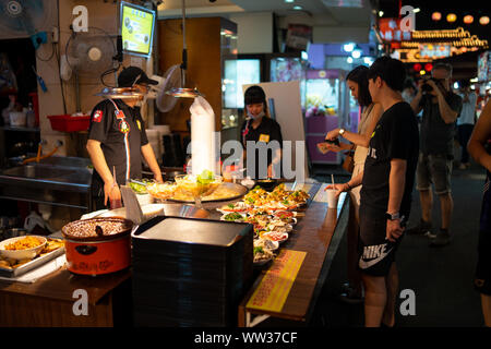Taipei: Customers buying food of a street food vendor. Street food stall selling a variety of different dishes at sidewalk buffet at a night market Stock Photo