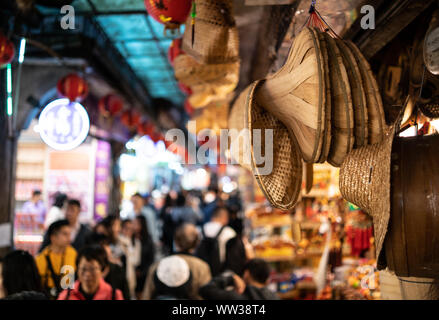 Straw and bamboo leaf hats hanging on ceiling of jiufen old street. Shop for traditional chinese hats with busy street in blurry background Stock Photo