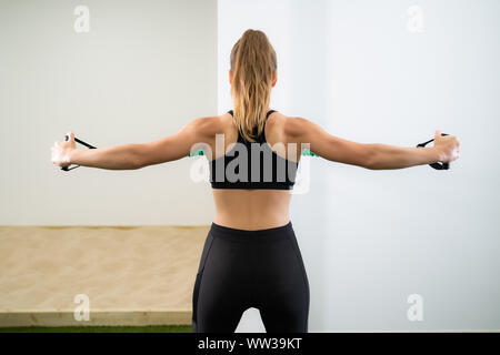 Rear view of a girl dressed in black clothes and blond hair doing a stretching exercise with a bracket embedded in the wall with a white wall in the b Stock Photo