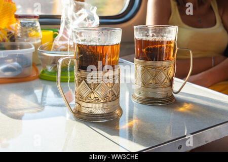 On the table in the train compartment are glasses with tea in metal cup holders. Stock Photo