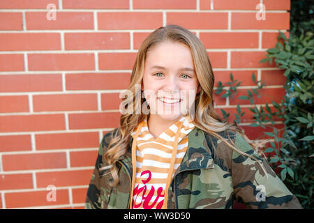 Happy teen girl with smiling by brick wall on sunny day Stock Photo