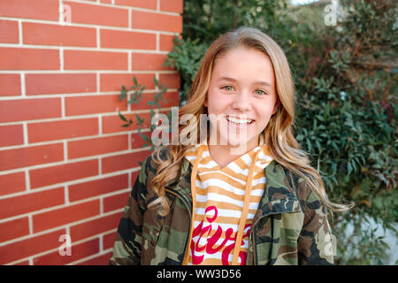 Happy teen girl smiling by brick wall on sunny day Stock Photo