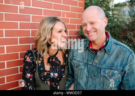 Happy smiling couple in front of brick wall on sunny day in California Stock Photo