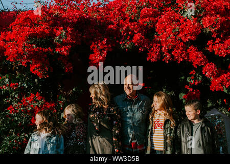 Smiling father with his family in front of red flowers on sunny day Stock Photo