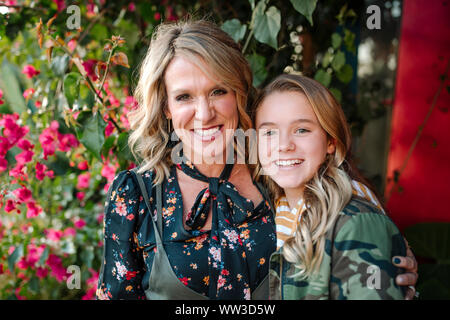 Smiling mother and daughter in front of red flowers on sunny day Stock Photo