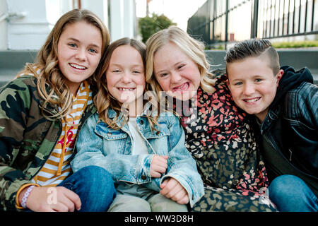 Smiling siblings hugging sister with Down Syndrome Stock Photo