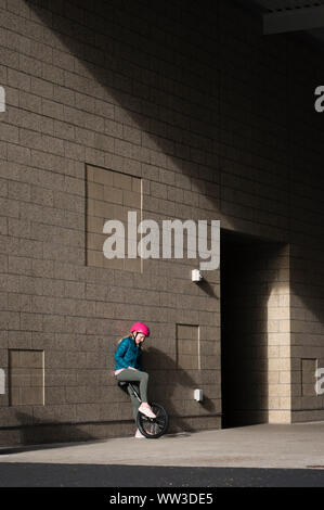 Girl in Pink Helmet Leaning Against Wall with Unicycle Stock Photo