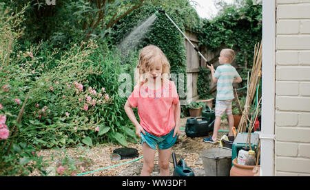 brother and sister playing with water in their English country garden Stock Photo