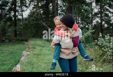 mother carrying her son through the forest whilst hiking on holiday Stock Photo