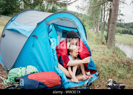 mother & son sat cuddling in a sleeping bag whist camping on vacation Stock Photo