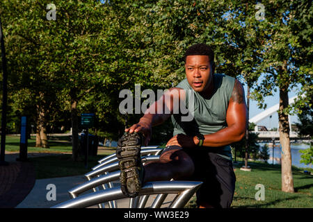 A man in athletic gear stretches in a city park Stock Photo