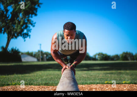 A strong athlete balances on single beam in park performing pushups Stock Photo