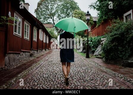 the back of a woman walking up a cobbled street with an umbrella Stock Photo