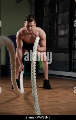 Muscular man with battle rope doing exercise in functional training gym Stock Photo