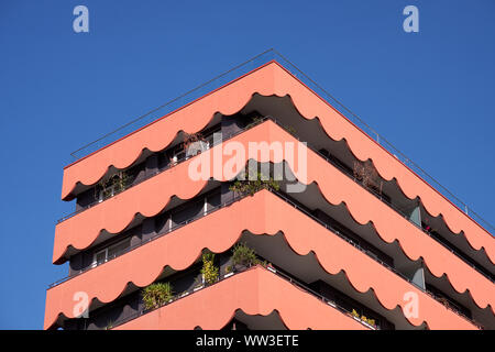 Close up Section of Red coloured apartment building with wavy lines balcony at angle.  View of top three floors Stock Photo