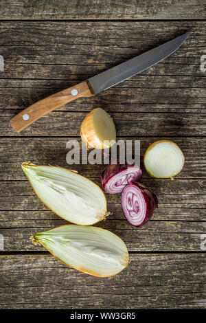 Halved fresh bulbs. Cut onions and knife on old wooden table. Top view. Stock Photo