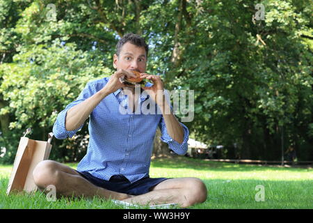 A Man enjoying his burger in a park Stock Photo