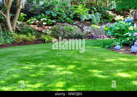 A beautiful backyard garden features a maintenance free lawn made of realistic looking artificial grass, a huge landscaping trend for small spaces. Stock Photo
