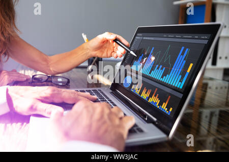 Close- Up Of Office Workers Analyzing Graph On Laptop With His Coworker Stock Photo