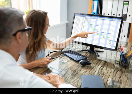 Mature Businesspeople Analyzing Gantt Chart And Calendar On Computer In Office Stock Photo