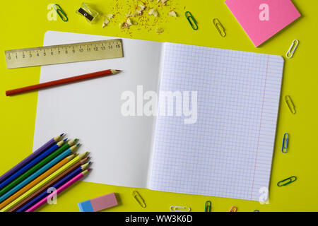 Notebook in a cage with a pencil, eraser, ruler, paper clips and other office supplies on a yellow background. Concept back to school. Place for text. Stock Photo