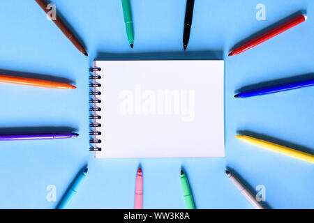 Open notepad and open multicolored markers on the blue background. Place for text. Concept back to school. Stock Photo