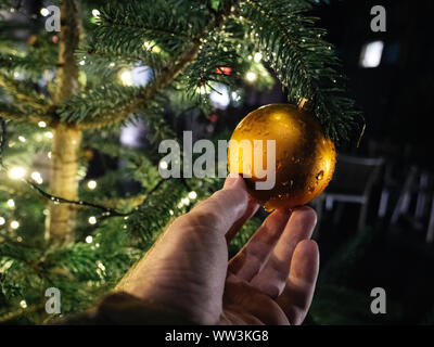 Man hand holding sparkling golden globe hanged on a tree with defocused blur bokeh in background Stock Photo